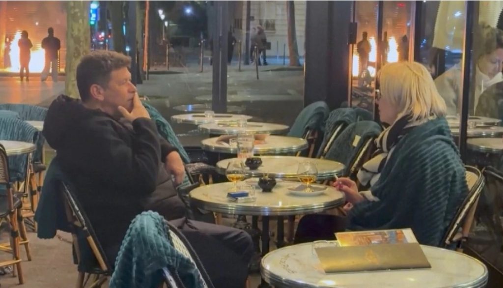 Σουρεαλιστικό βίντεο από το Παρίσι: Ζευγάρι απολαμβάνει το ποτό του σε καφετέρια, ενώ δίπλα του οι δρόμοι έχουν πάρει φωτιά